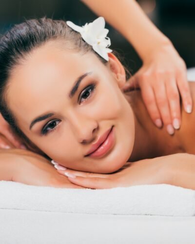 woman relaxing and having massage at spa salon and looking at camera